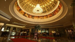 Un vaste hall d’entrée agrémenté d’un grand lustre somptueux, d’une composition florale centrale et d’un comptoir d’accueil.