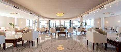 Un hall amplio con suelo de mármol pulido, muebles modernos y grandes ventanales que dejan entrar luz natural.