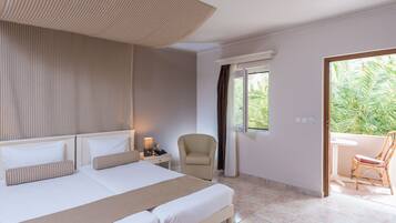 A hotel room with a large bed, a chair, a small table, and a view of greenery outside.