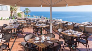 An outdoor dining area with tables and chairs, overlooking a body of water. - Athina Palace Resort & Spa (Malevizi)