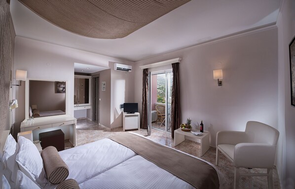 Habitación de hotel con una cama grande, un escritorio con televisor de pantalla plana, una silla, una mesita con un cesto y una ventana con cortinas.