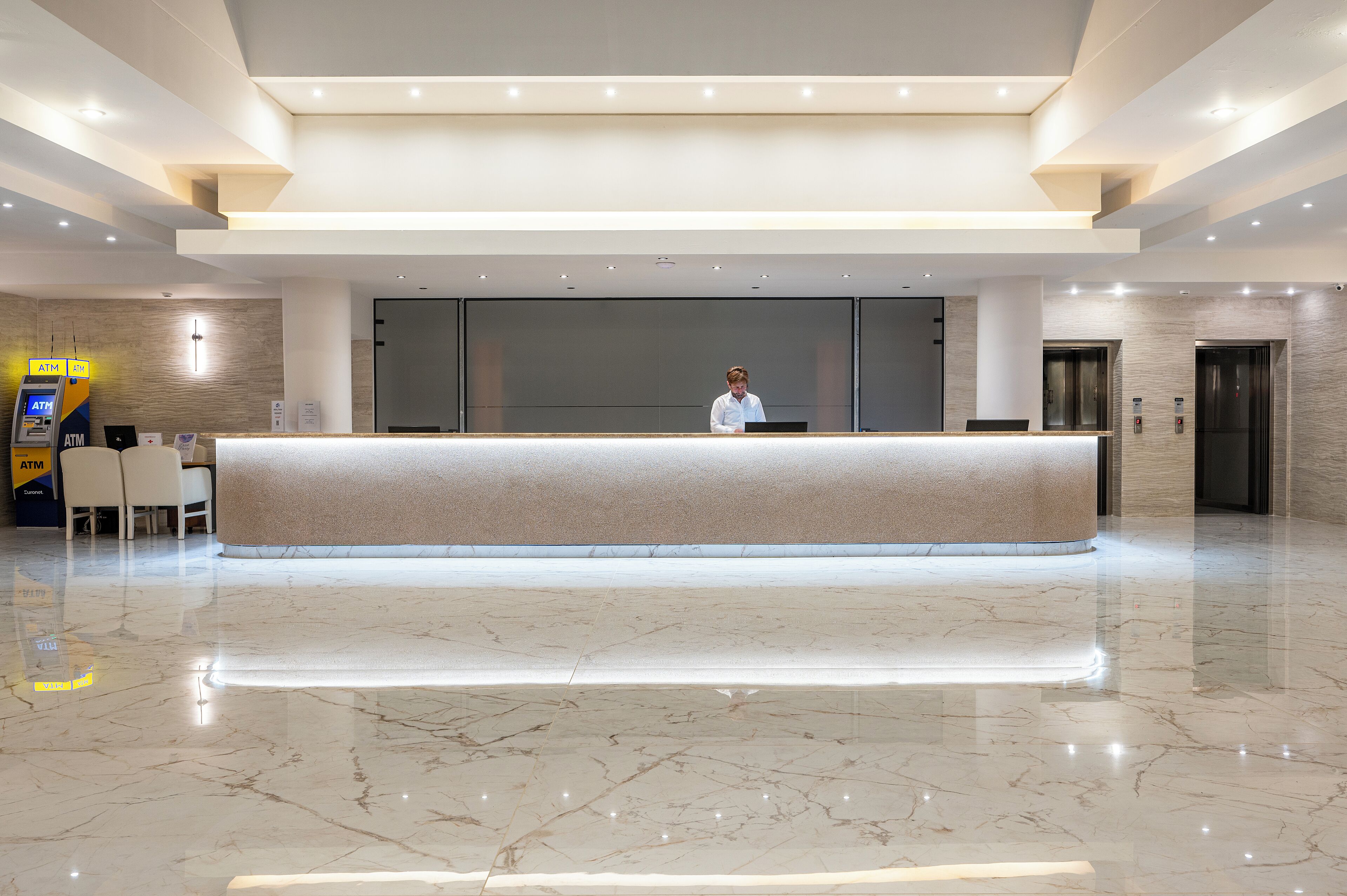 A modern hotel reception area with a marble floor, a reception desk, and an ATM machine.