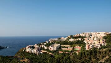 Una zona residencial costera con edificios modernos, vista despejada al mar y un terreno con colinas.