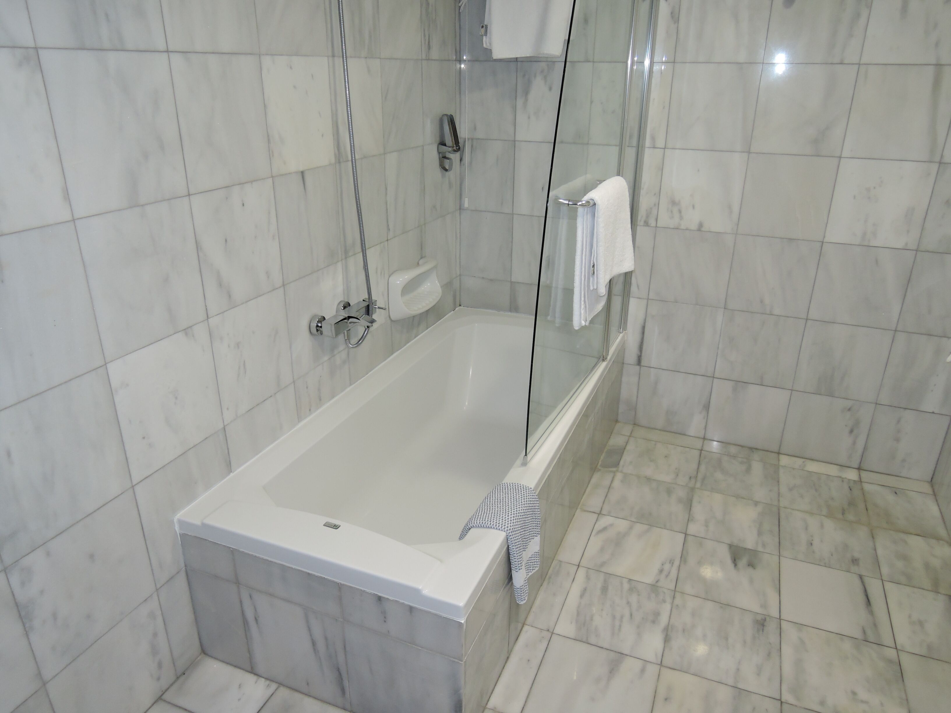 A modern bathroom with a glass-enclosed bathtub, a handheld showerhead, and a built-in soap dish.