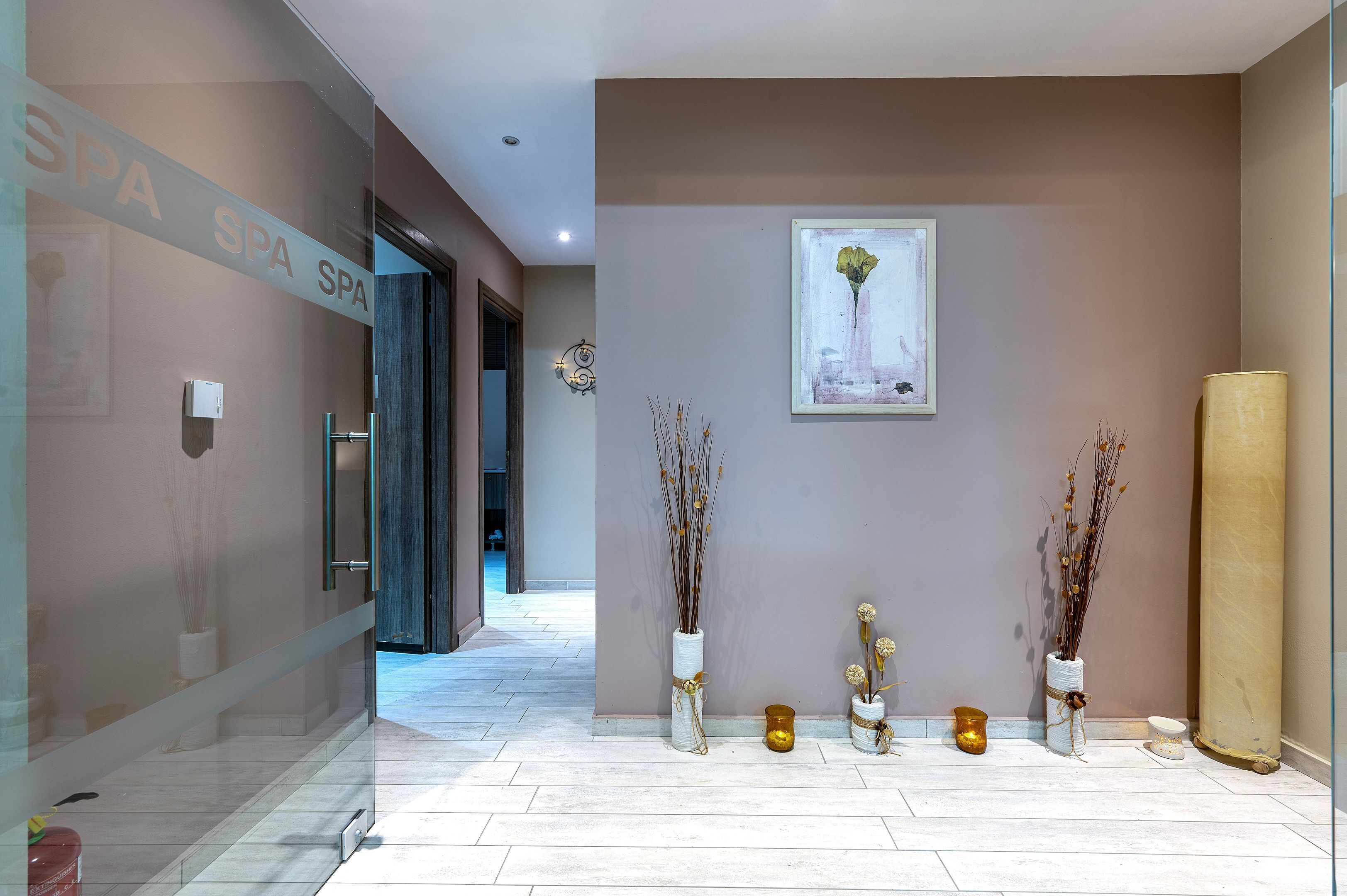 A modern spa entrance with a glass door, a sign reading "SPA SPA SPA," and decorative vases with dried plants.