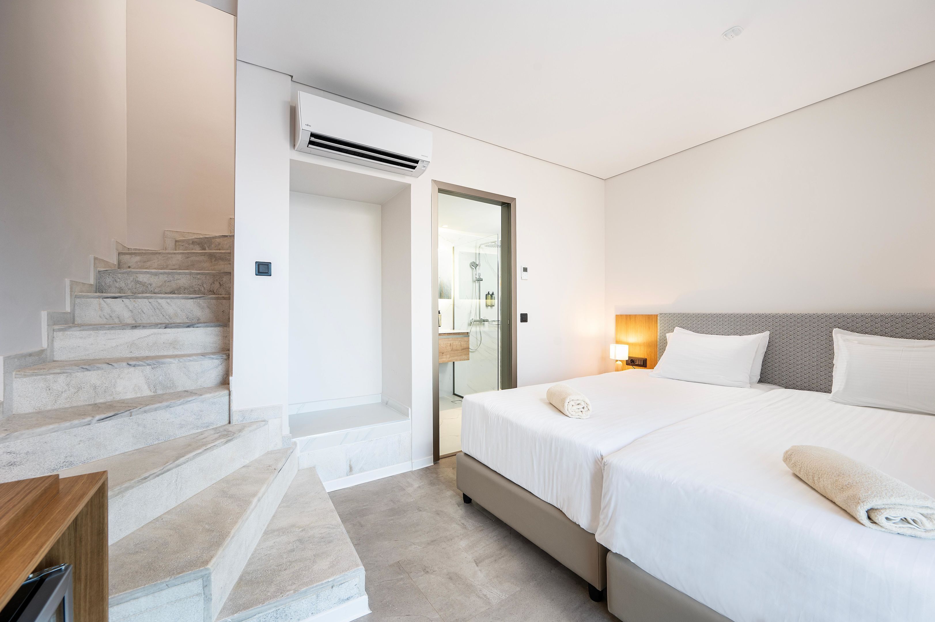 A modern hotel room with a marble staircase, a large bed with white linens, and a bathroom with a glass shower enclosure.