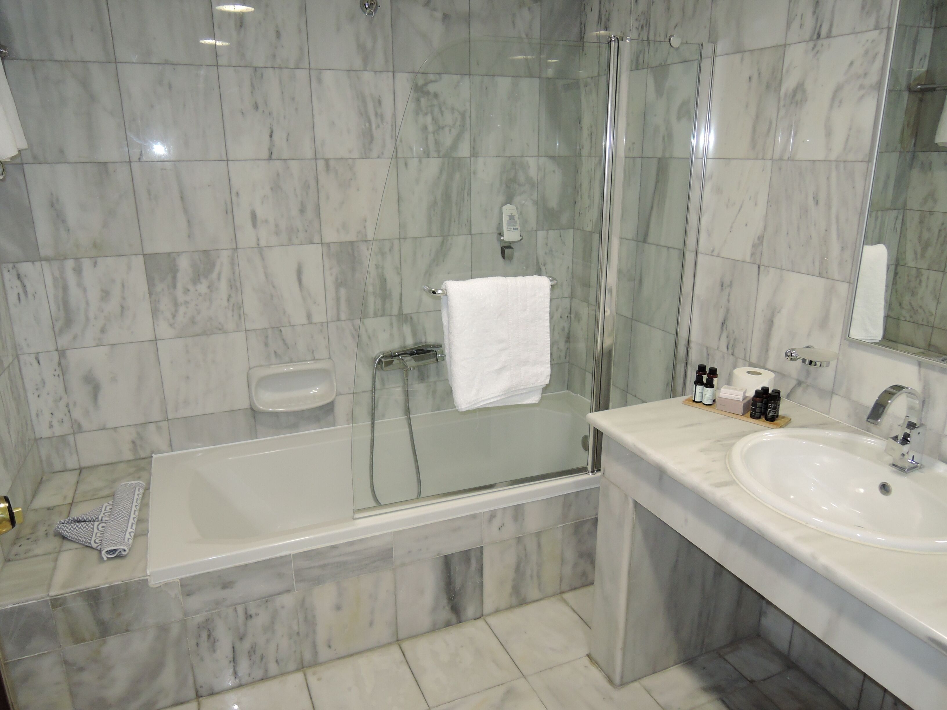A modern bathroom with a glass-enclosed shower, a bathtub, and a sink with toiletries.