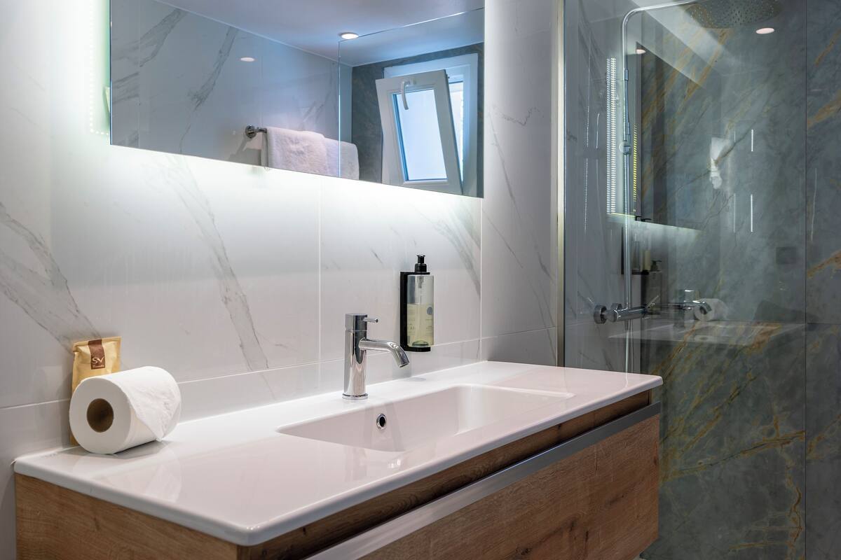 A bathroom with a marble sink, a mirror, and a glass shower enclosure.