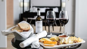 A dining table with a bottle of wine, two glasses of red wine, a plate of cheese, crackers, and bread. - Alentejo Marmoris Hotel & Spa, (Vila Vicosa)