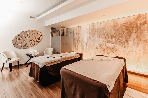 Un cuarto de spa con dos camillas de masaje, una silla blanca y una pared de piedra.