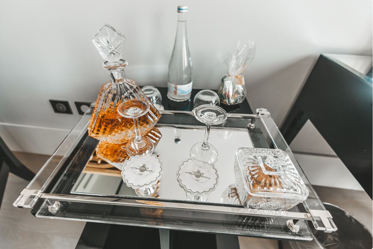 A clear glass tray with various glassware and bottles on a reflective surface.