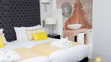 Habitación de hotel con una cama grande, una mesita de noche con lámpara, un espejo en la pared y un baño con lavamanos y un espejo amplio.