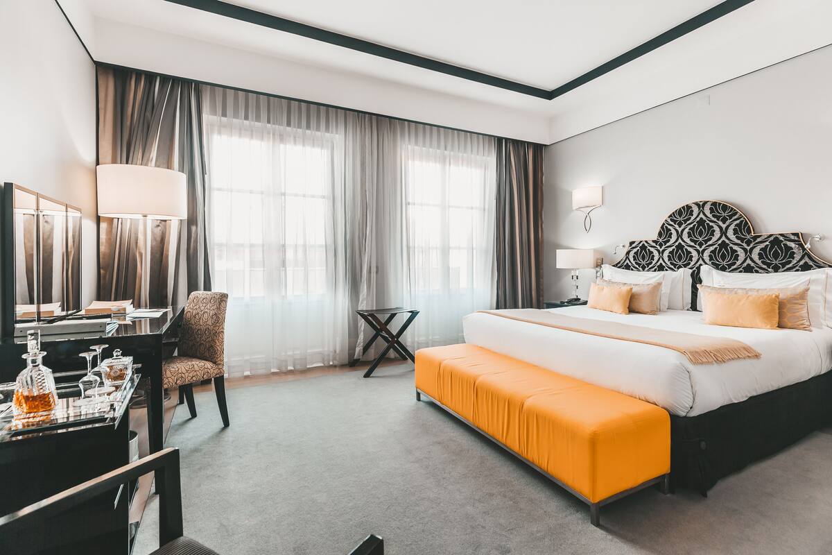 A hotel room with a bed, a desk, a chair, a lamp, and a window with curtains.