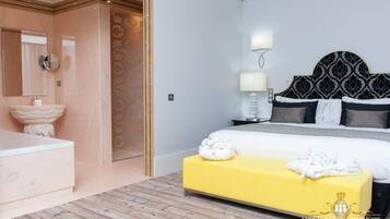 A modern hotel room with a large bed, a yellow bench, a bathroom with a large sink, and a mirror.