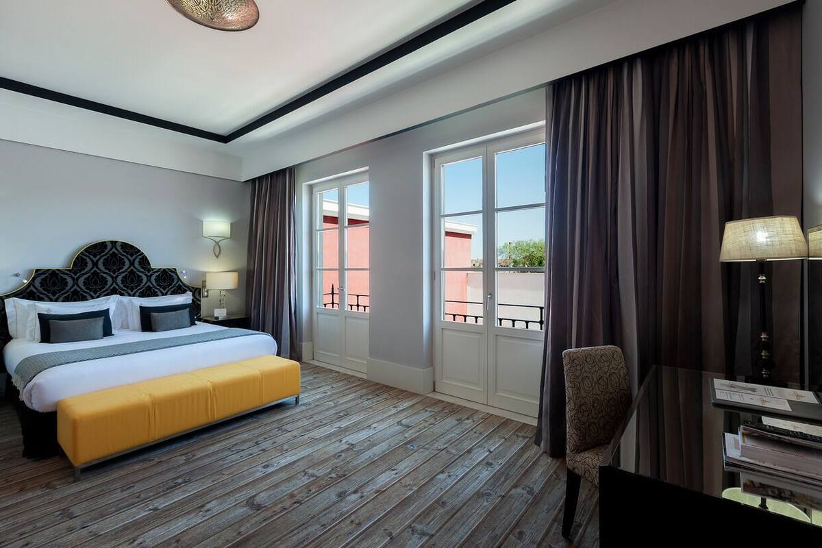 A hotel room with a large bed, a desk, a chair, and a view of the outside.