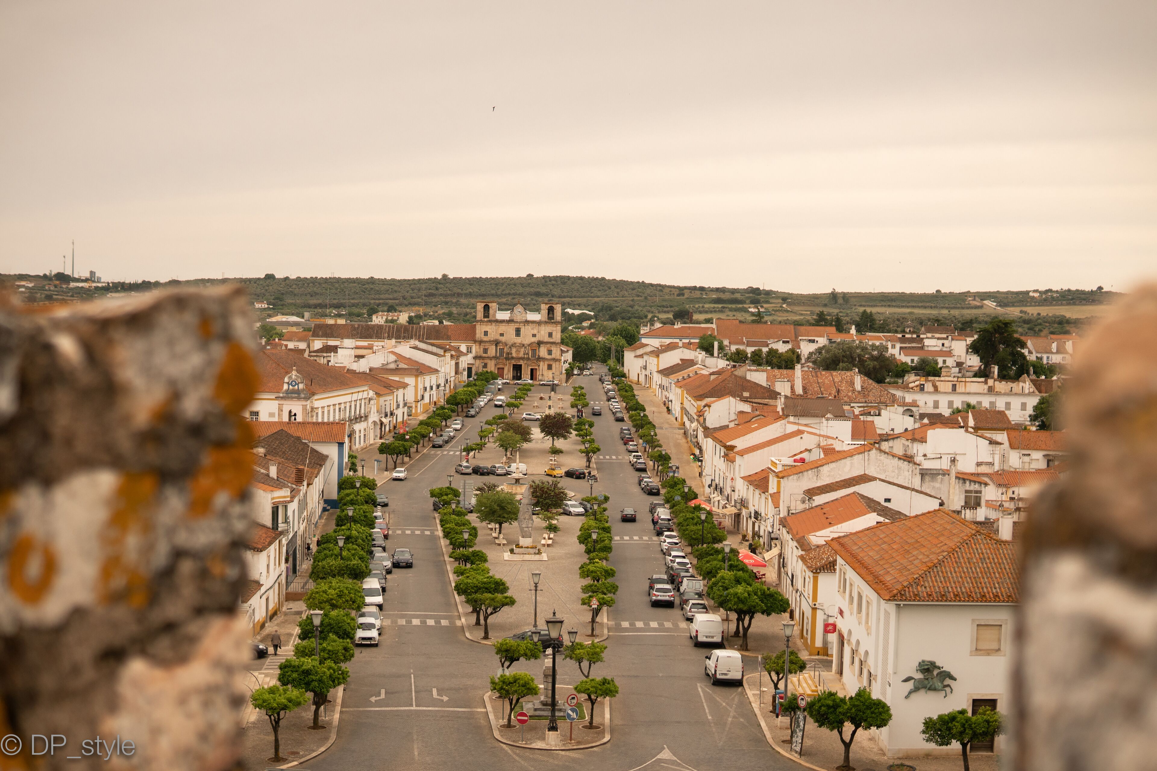 A street view of a town with buildings, trees, and a central square.