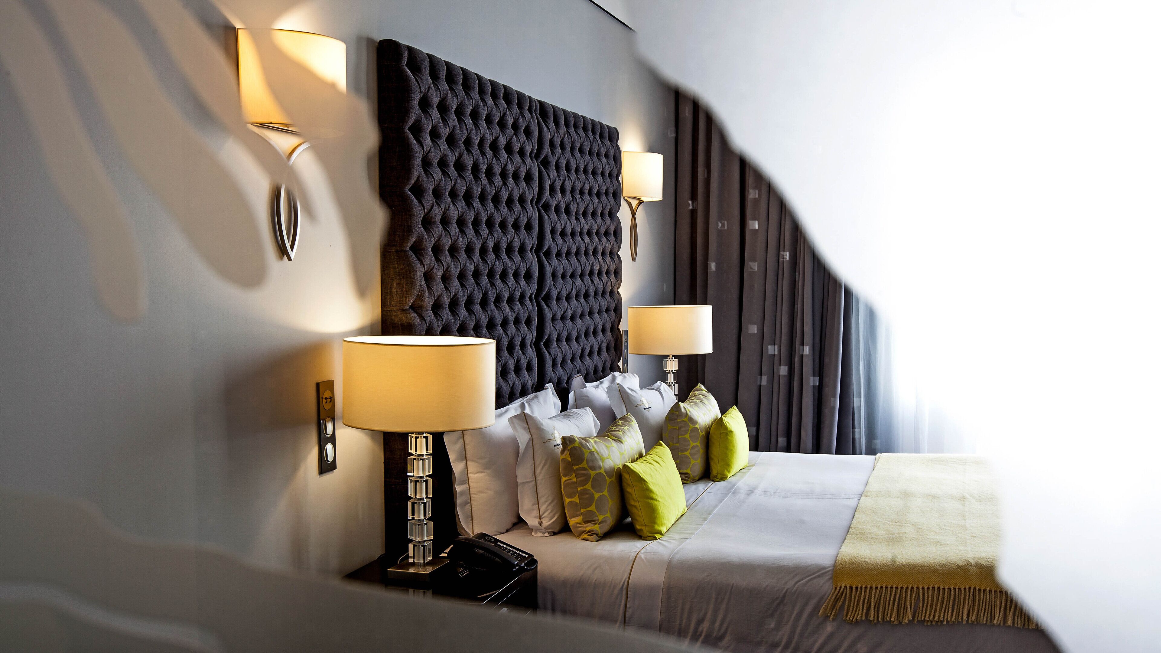 Un dormitorio moderno con cabecera capitonada, dos lámparas de noche, un televisor de pantalla plana y una variedad de almohadas.