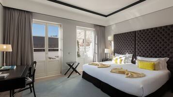 A hotel room with a large bed, a desk with a chair, a piano, and a view of the outside.