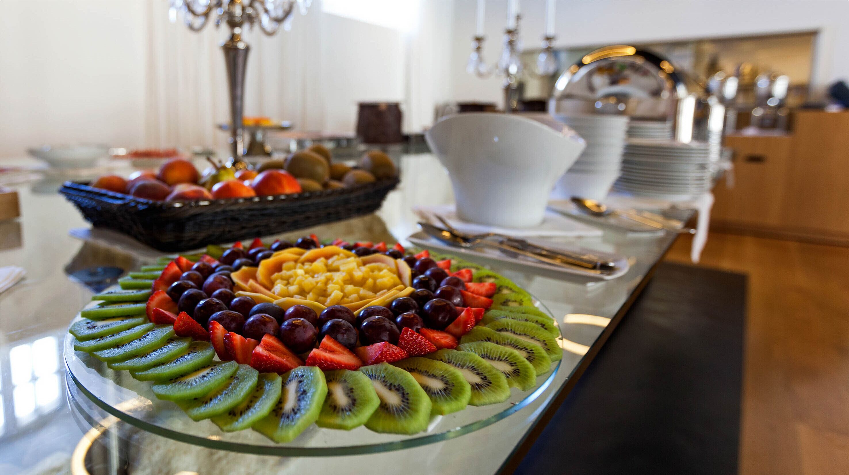 Une assiette de fruits est posée sur une table en verre, et elle contient une variété de fruits, notamment des fraises, des raisins et des tranches de kiwi.