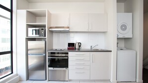 A modern kitchen with white cabinets, a stainless steel refrigerator, a microwave, an oven, and a dishwasher.