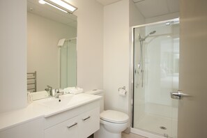 Une salle de bain moderne avec un lavabo, un miroir et des toilettes blancs, ainsi qu’un espace douche fermé par des parois de verre.