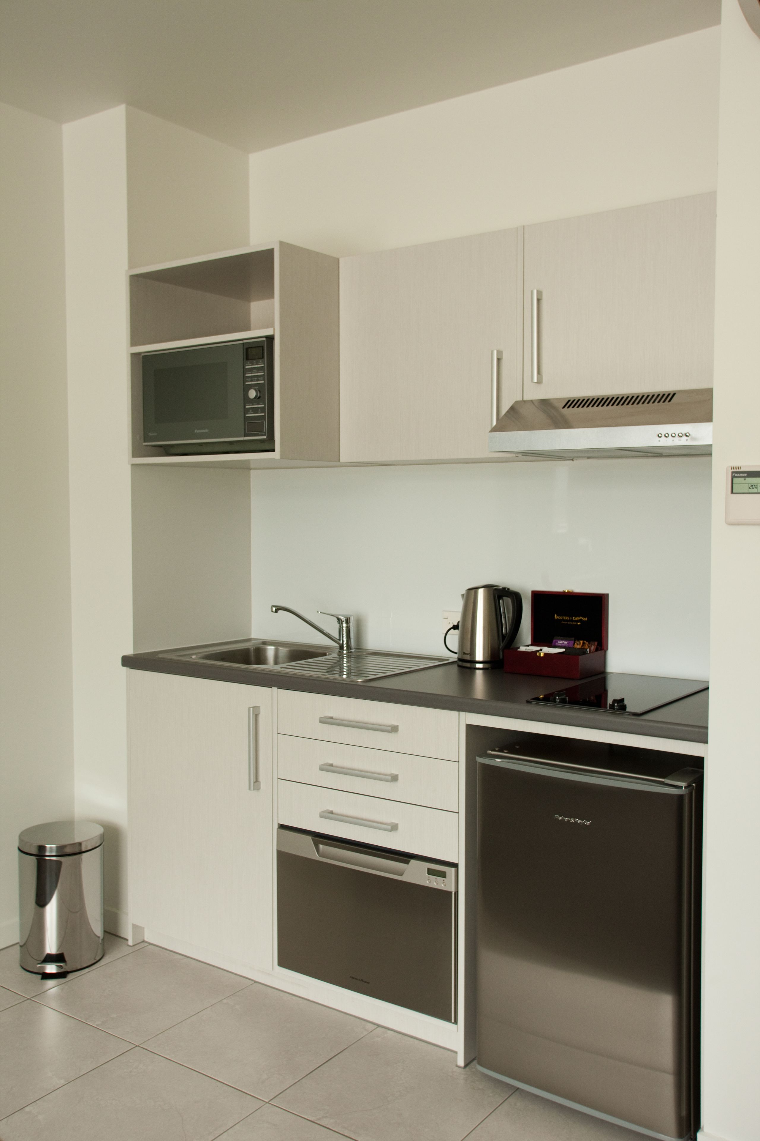 A compact kitchen with a microwave, sink, coffee maker, and a built-in dishwasher.