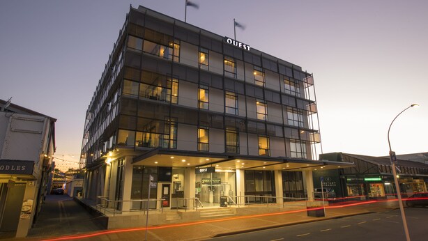 A modern hotel with a prominent "QUEST" sign, multiple floors, and a covered entrance area.