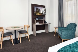A hotel room with a bed, a desk with a computer, a chair, a small table, and a view of a building through the window. - Quest Rotorua Central (Rotorua)