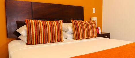 A neatly made bed with striped pillows and a white comforter, set against an orange wall.
