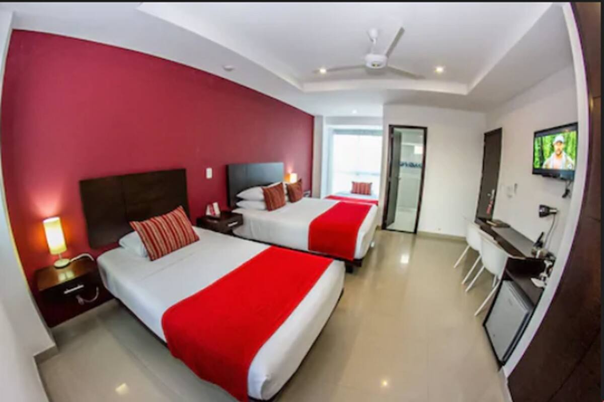 A hotel room with two beds, a TV, a desk, and a view of the sea.