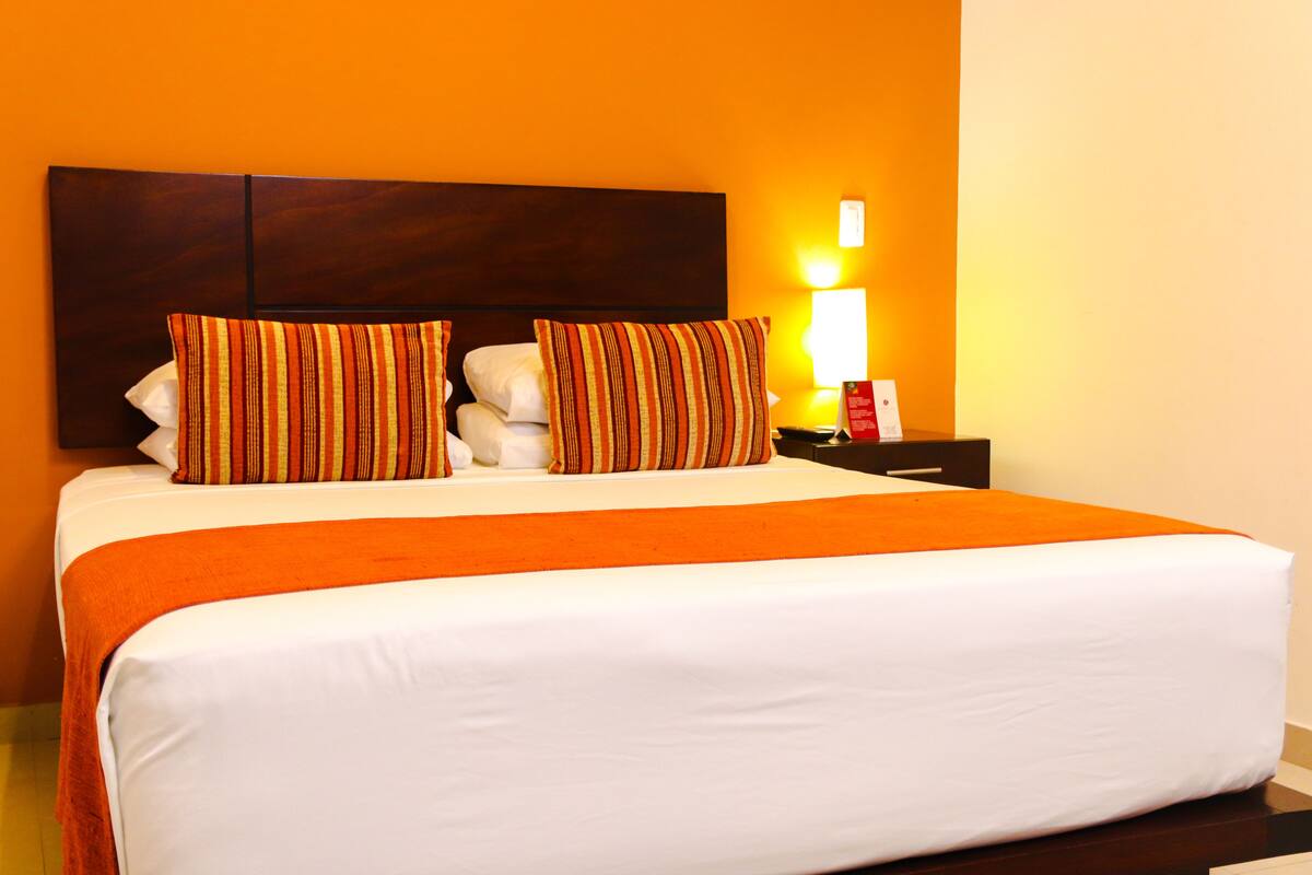 A hotel room with a large bed, orange bedding, and a wooden headboard.