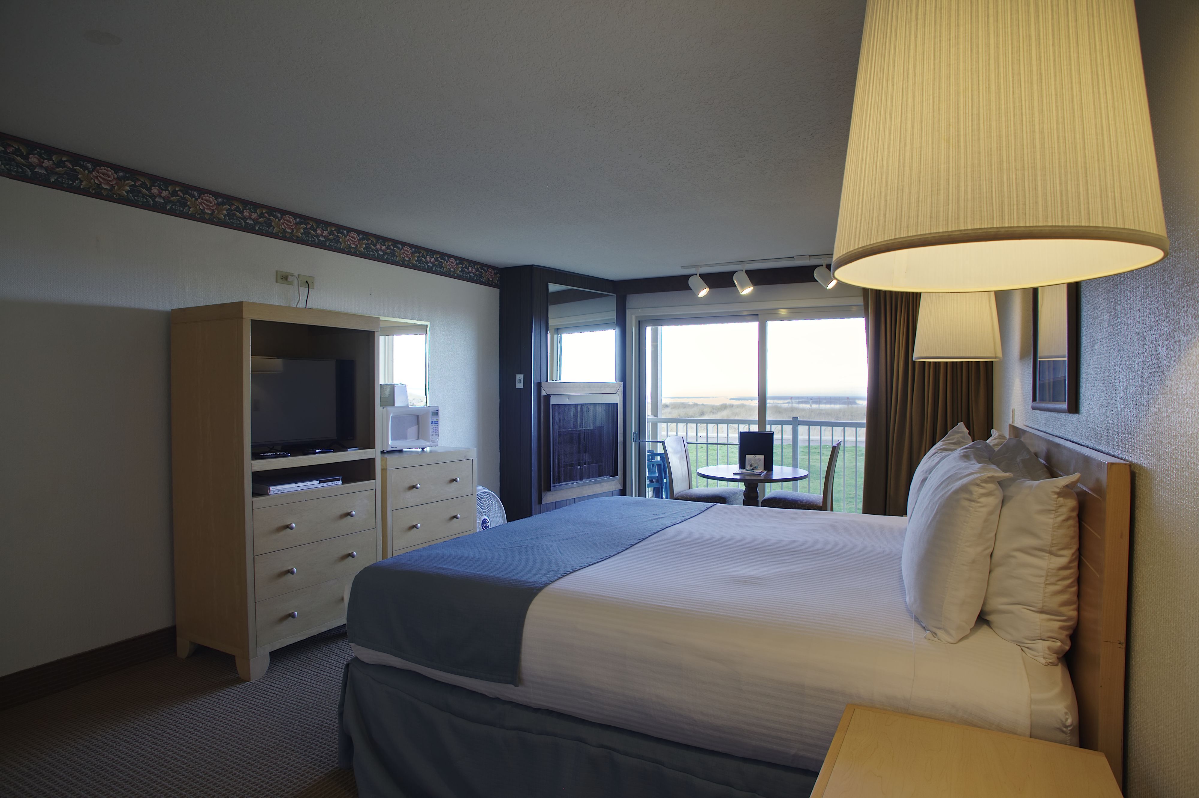 A hotel room with a bed, a TV, a dresser, and a balcony with a view.