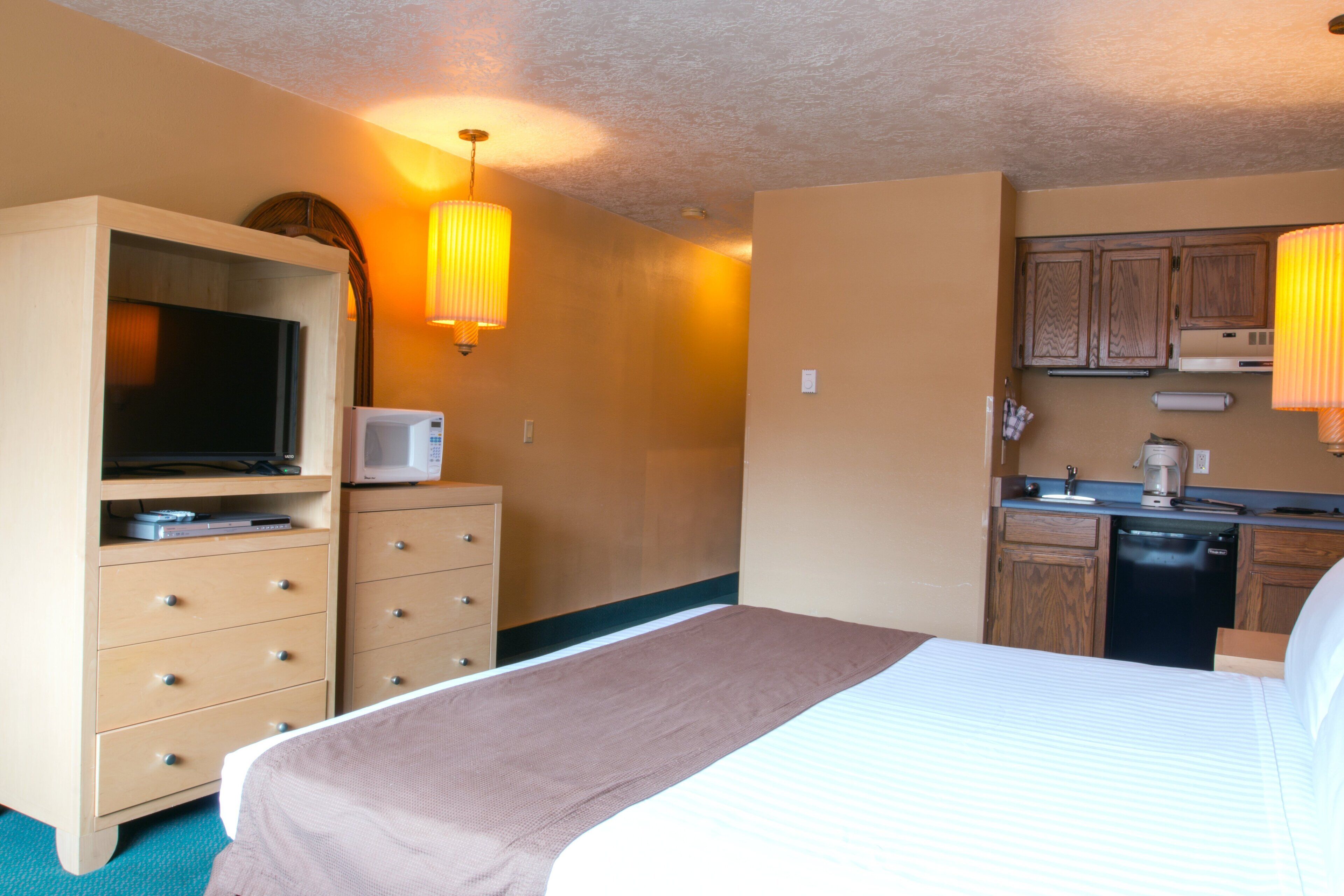 Een hotelkamer met een bed, een dressoir, televisie, magnetron en kitchenette.