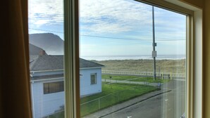 A coastal view from a window overlooking a grassy area, a road, and a beach with waves.