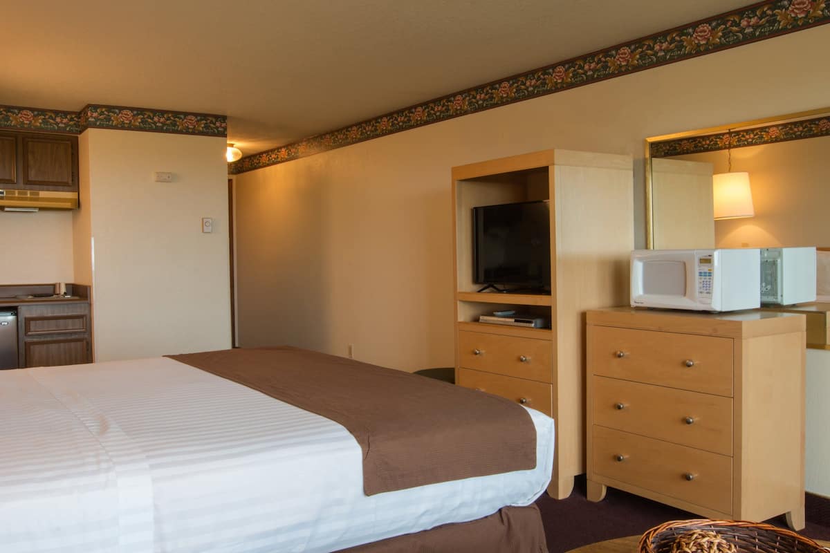 A hotel room with a bed, a dresser, a microwave, a television, and a small kitchen area.