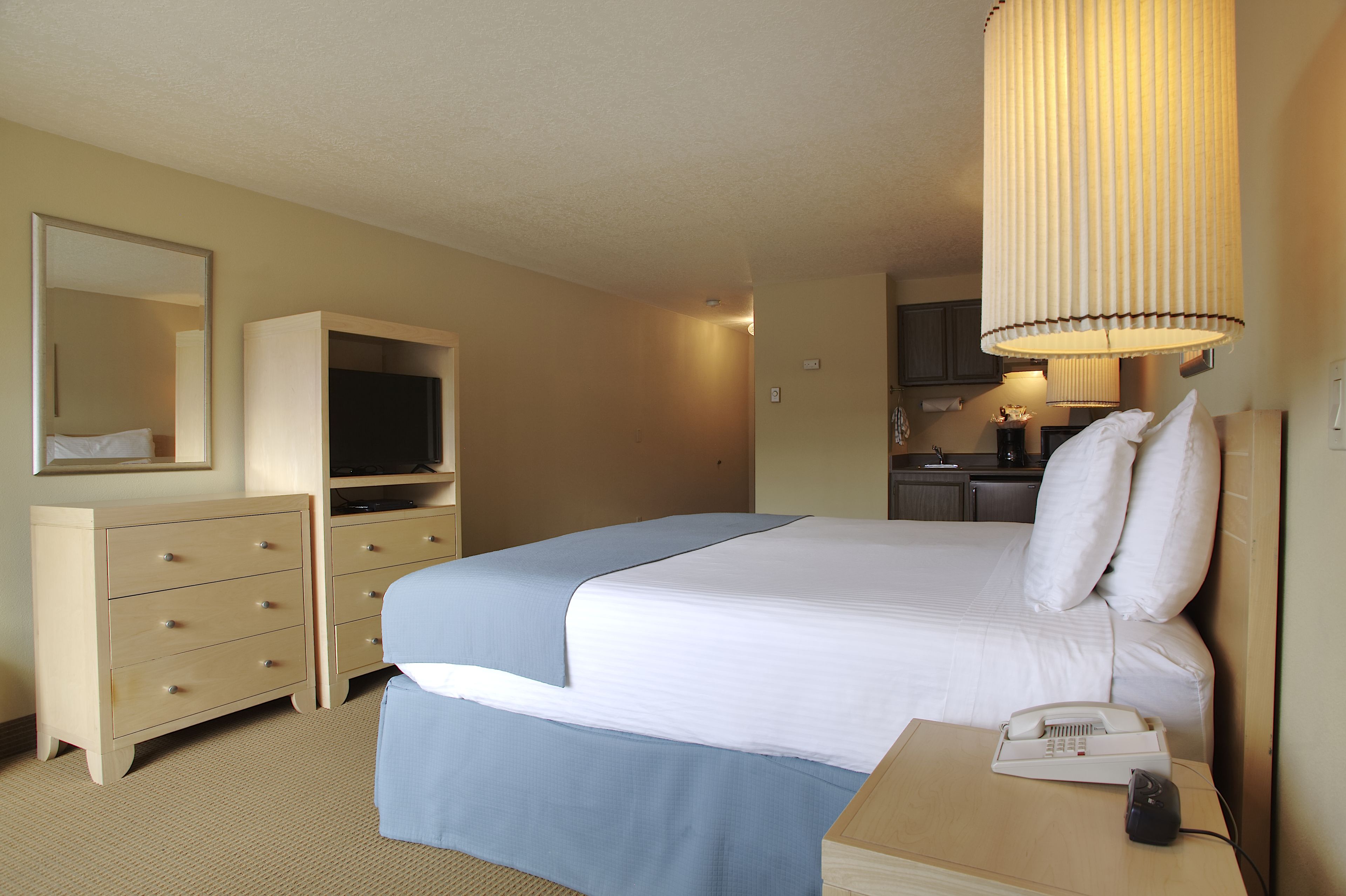 Ein Hotelzimmer mit Bett, Schreibtisch mit Telefon, Fernseher, Spiegel und einer Küchenzeile.