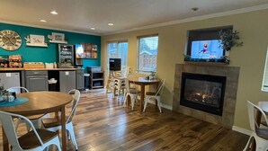 A spacious living room with a fireplace, a dining area with a wooden table and white chairs, a kitchen with teal walls and modern appliances, and a large window providing natural light. - Hi-Tide Oceanfront Inn (Seaside)