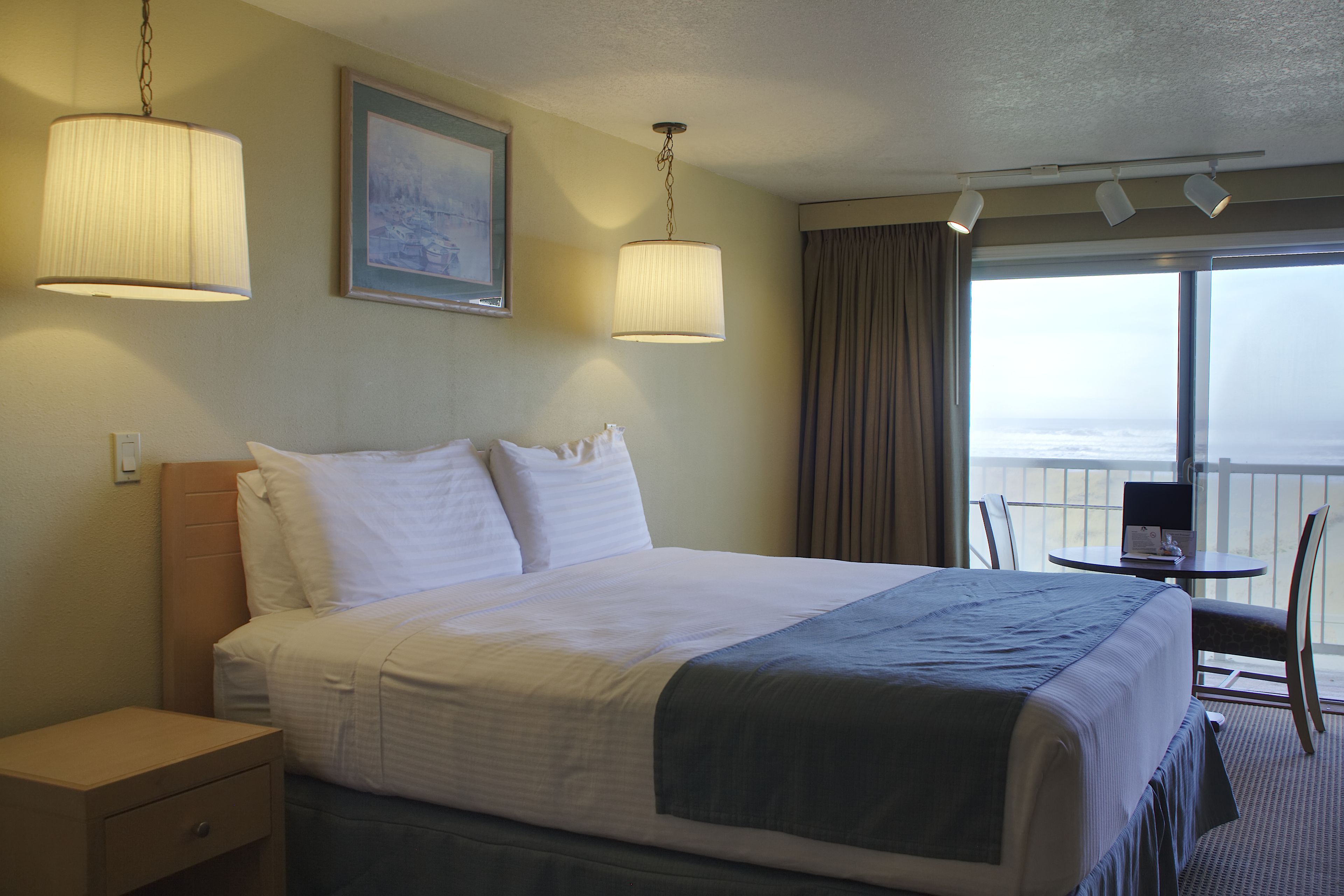 A hotel room with a bed, bedside table, lamp, and a view of the ocean through a large window.