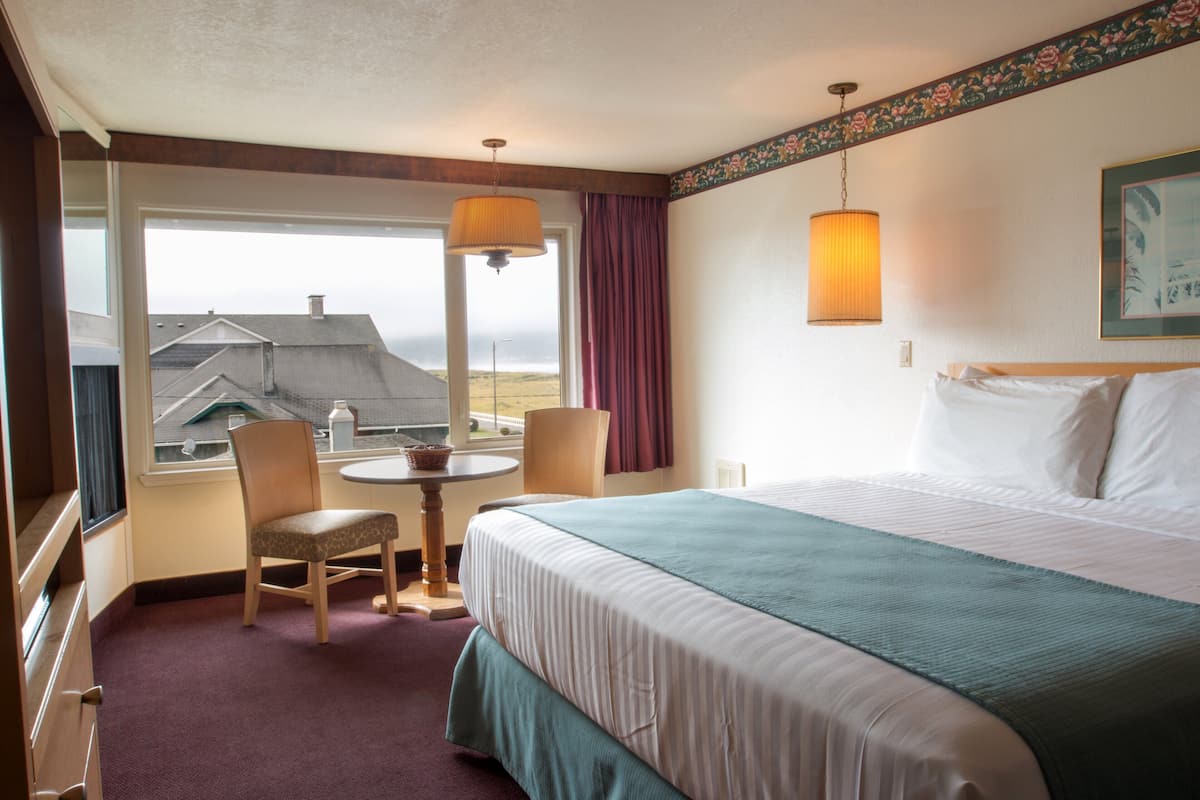 A hotel room with a bed, a chair, a small table, and a window with a view of buildings.