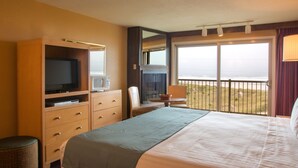 A hotel room with a bed, a television, a desk, and a window with a view of the beach. - Hi-Tide Oceanfront Inn (Seaside)