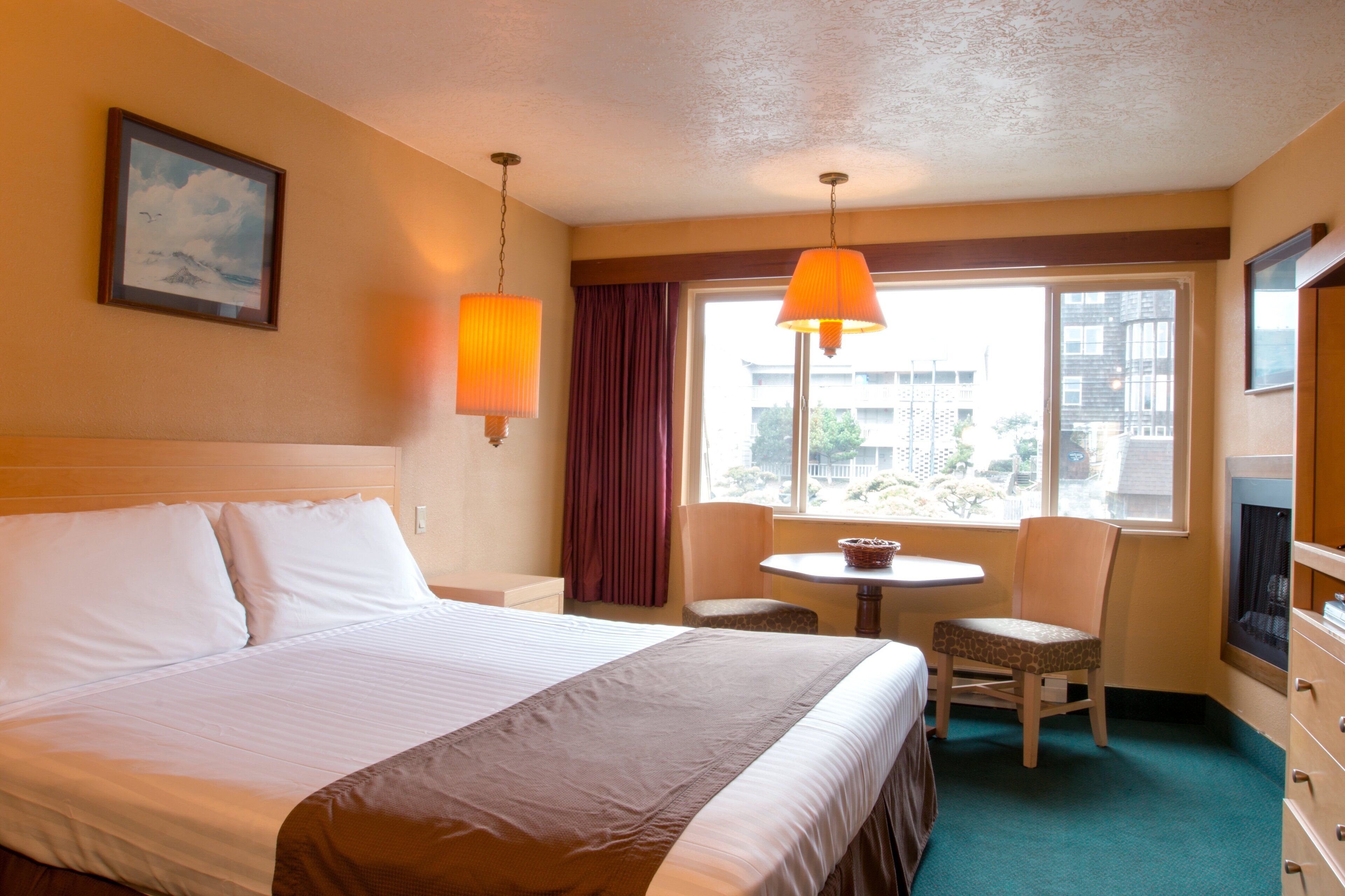 Une chambre d’hôtel avec un lit, un bureau, deux chaises, une fenêtre donnant sur un paysage agréable et une lampe.