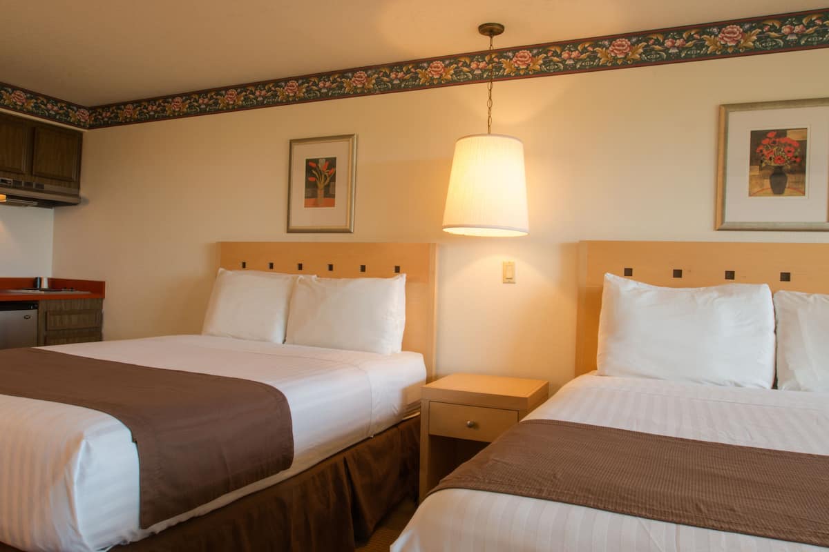 A hotel room with two beds, a nightstand, a lamp, and a framed picture on the wall.