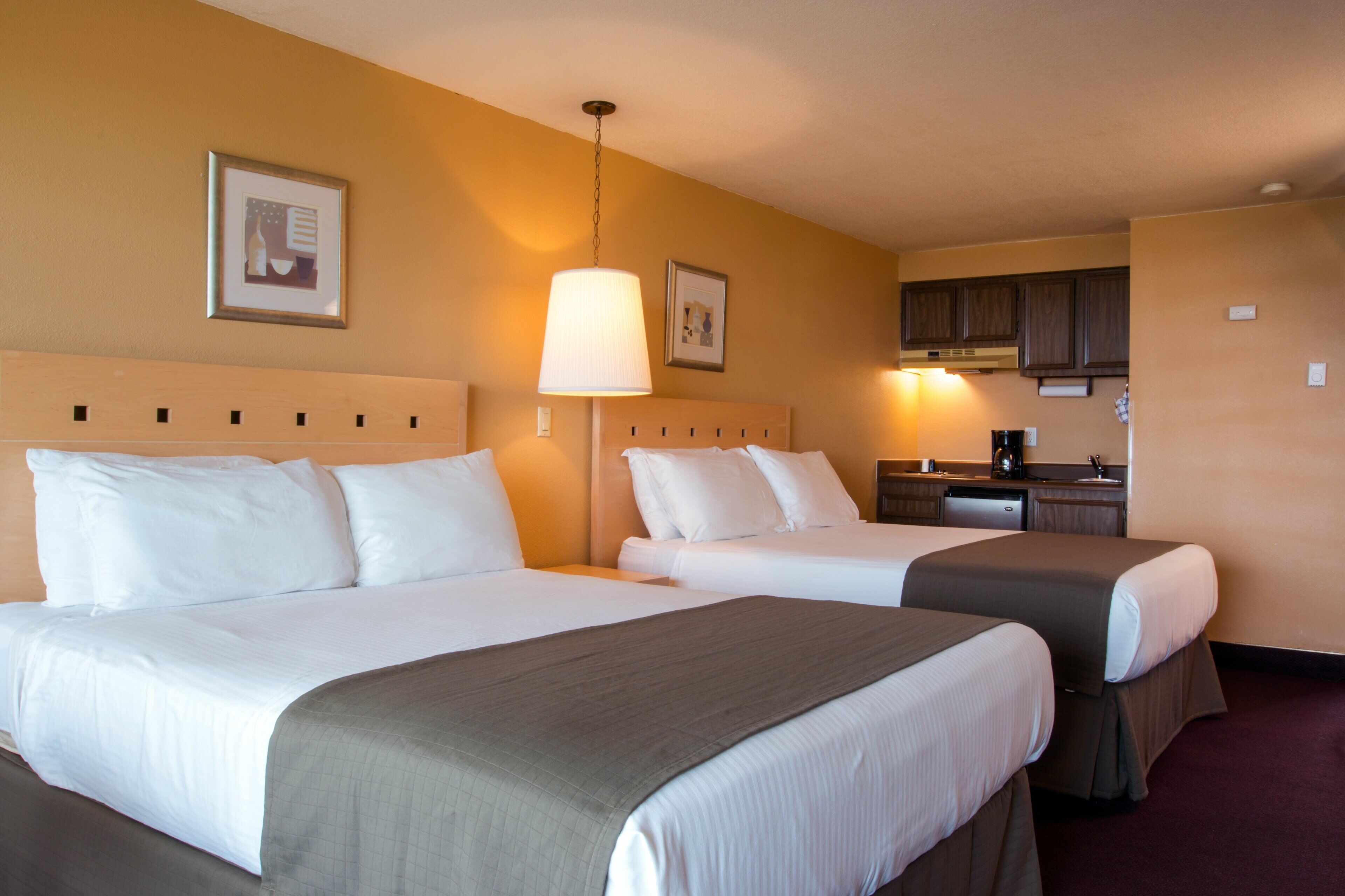 A hotel room with two beds, a desk, and a kitchenette.