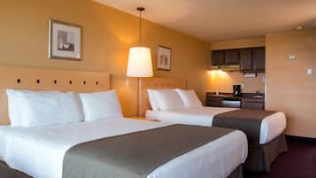 A hotel room with two beds, a desk, and a kitchenette.