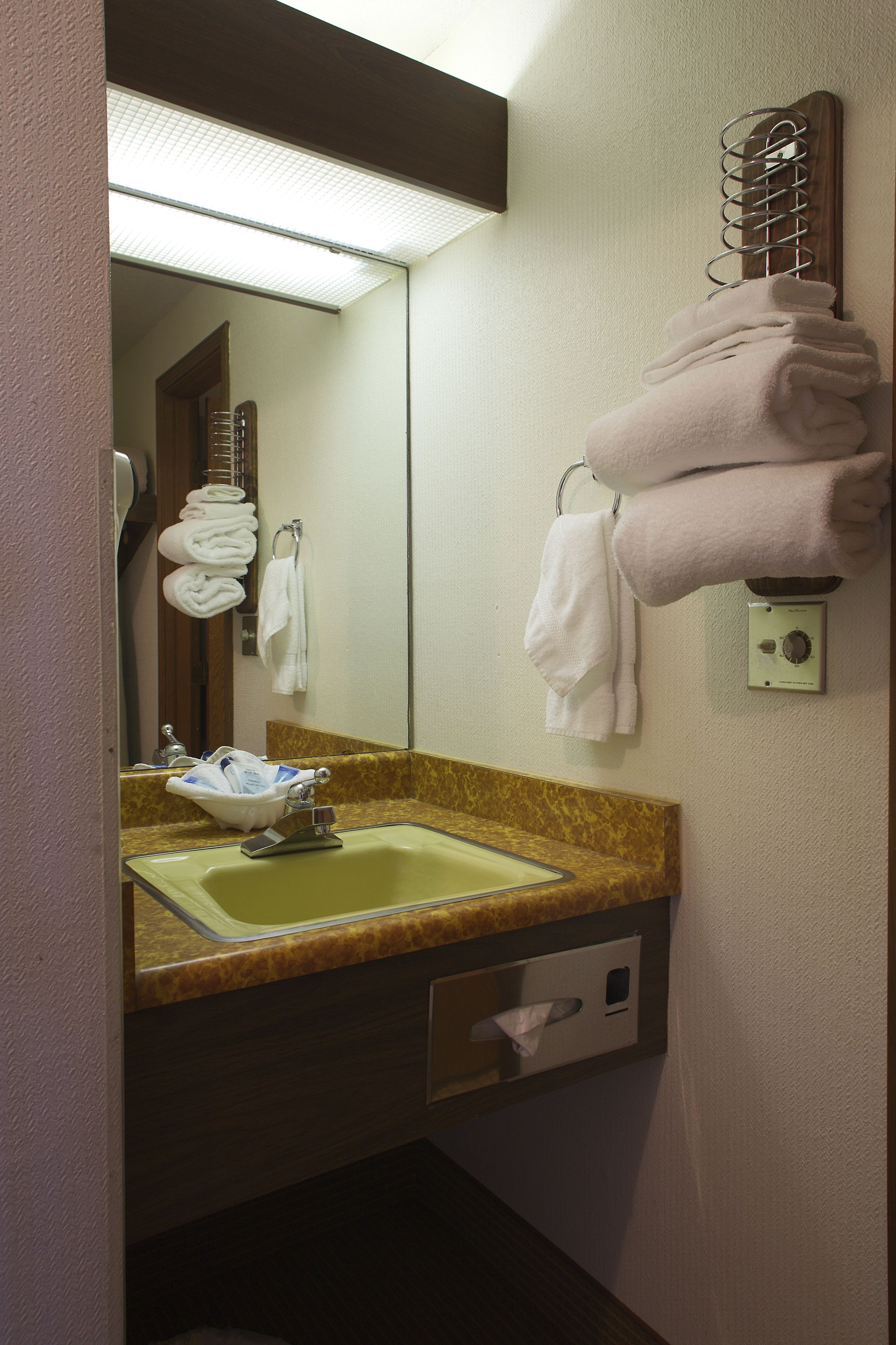 A hotel bathroom with a sink, mirror, towel rack, and a towel warmer.