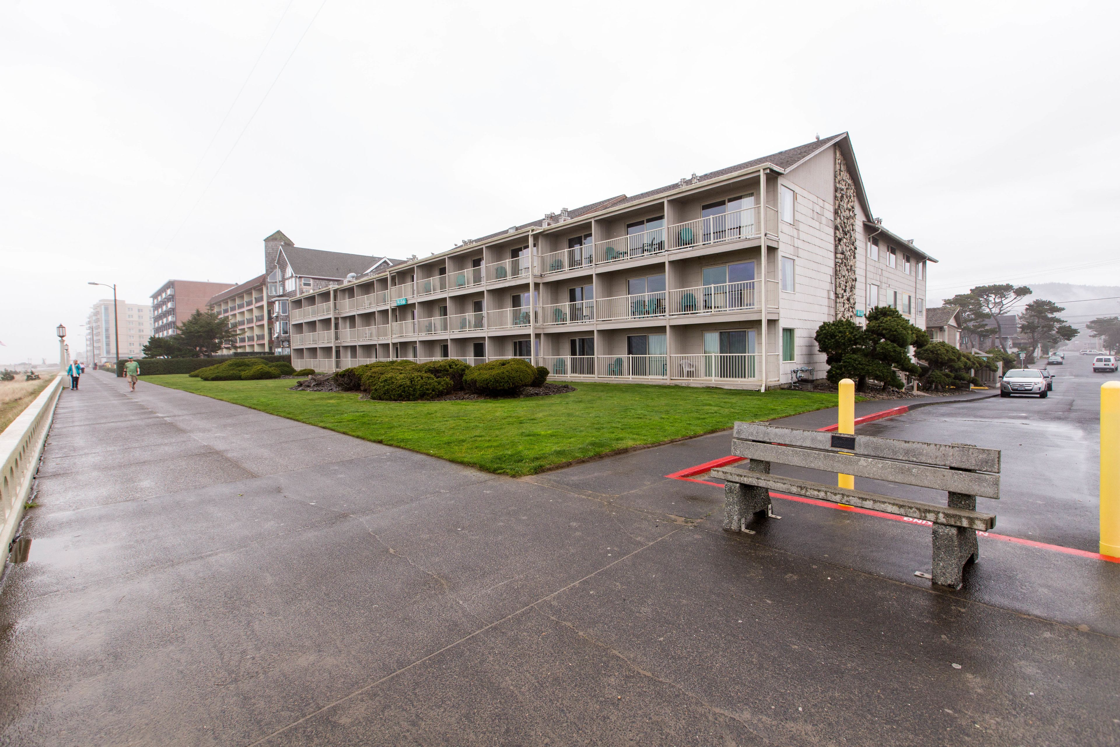 A multi-story building with balconies, a paved walkway, and a bench.