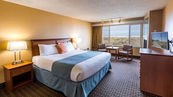 A hotel room with a large bed, a desk, a chair, and a TV.