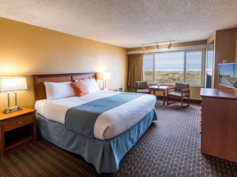 A hotel room with a large bed, a desk, a chair, and a TV.
