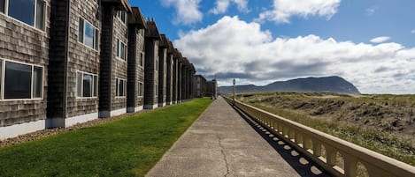 A coastal road with a sidewalk, buildings with shingled facades, and a clear sky.