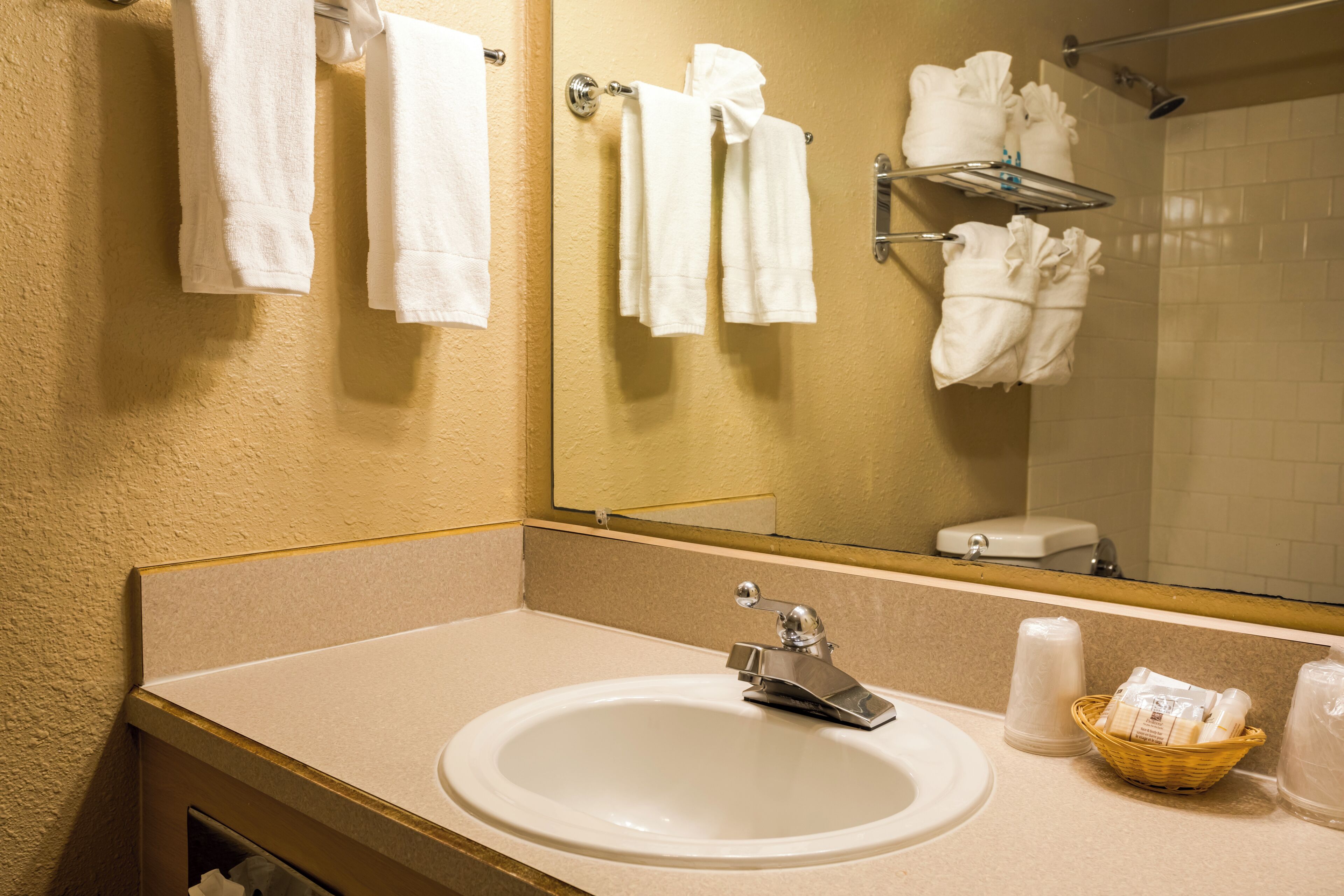 A bathroom with a sink, mirror, towel rack, and a basket of toiletries.